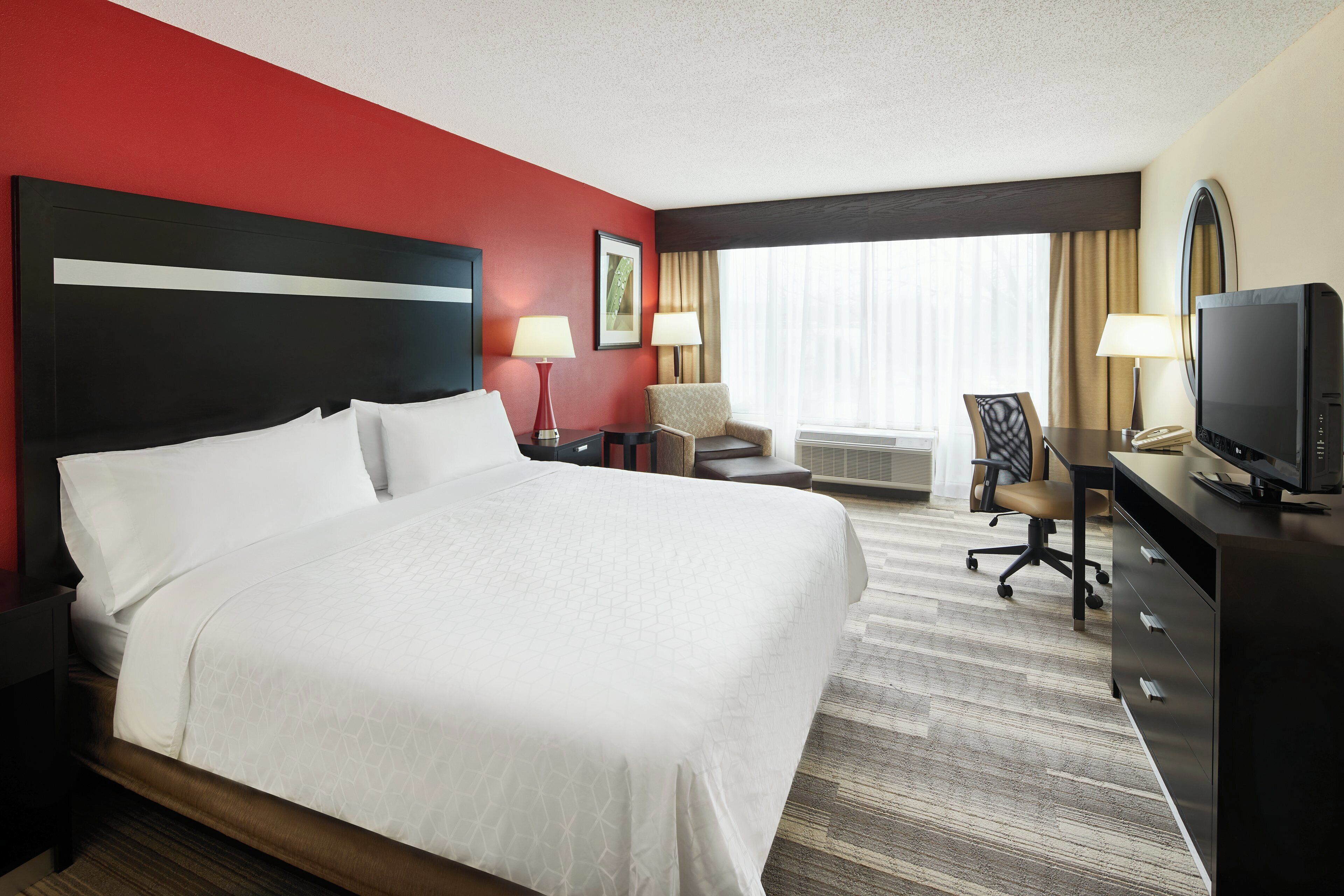 Een hotelkamer met een groot bed, een bureau met een computer, een stoel, een televisie en een raam met gordijnen.