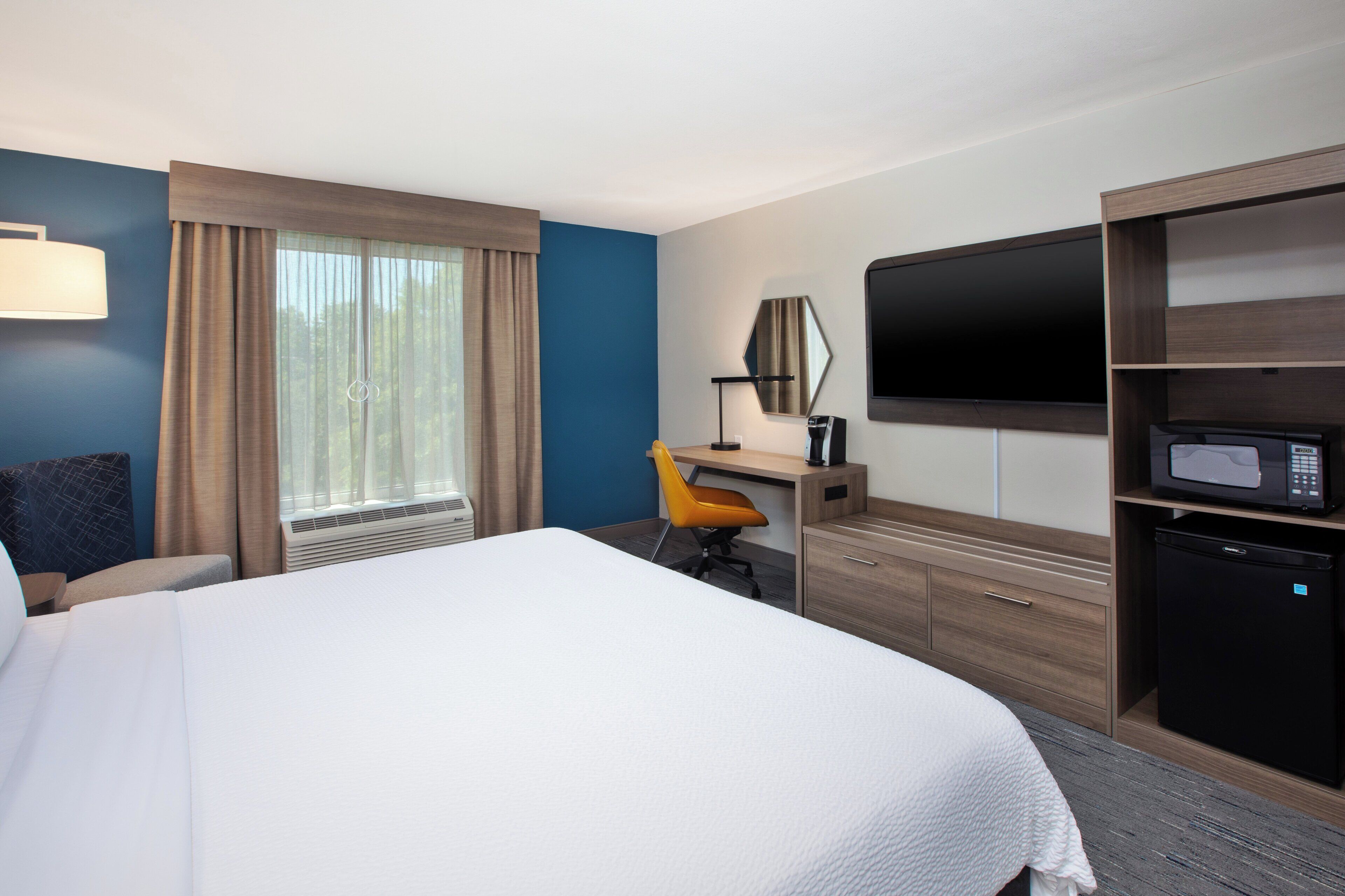 Une chambre d’hôtel avec un grand lit, un bureau avec une chaise, une télévision, un four à micro-ondes et un réfrigérateur.