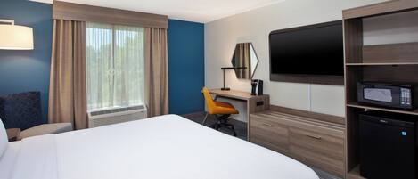 Quarto de hotel com uma cama grande, uma escrivaninha com cadeira, uma televisão, micro-ondas e frigorífico.