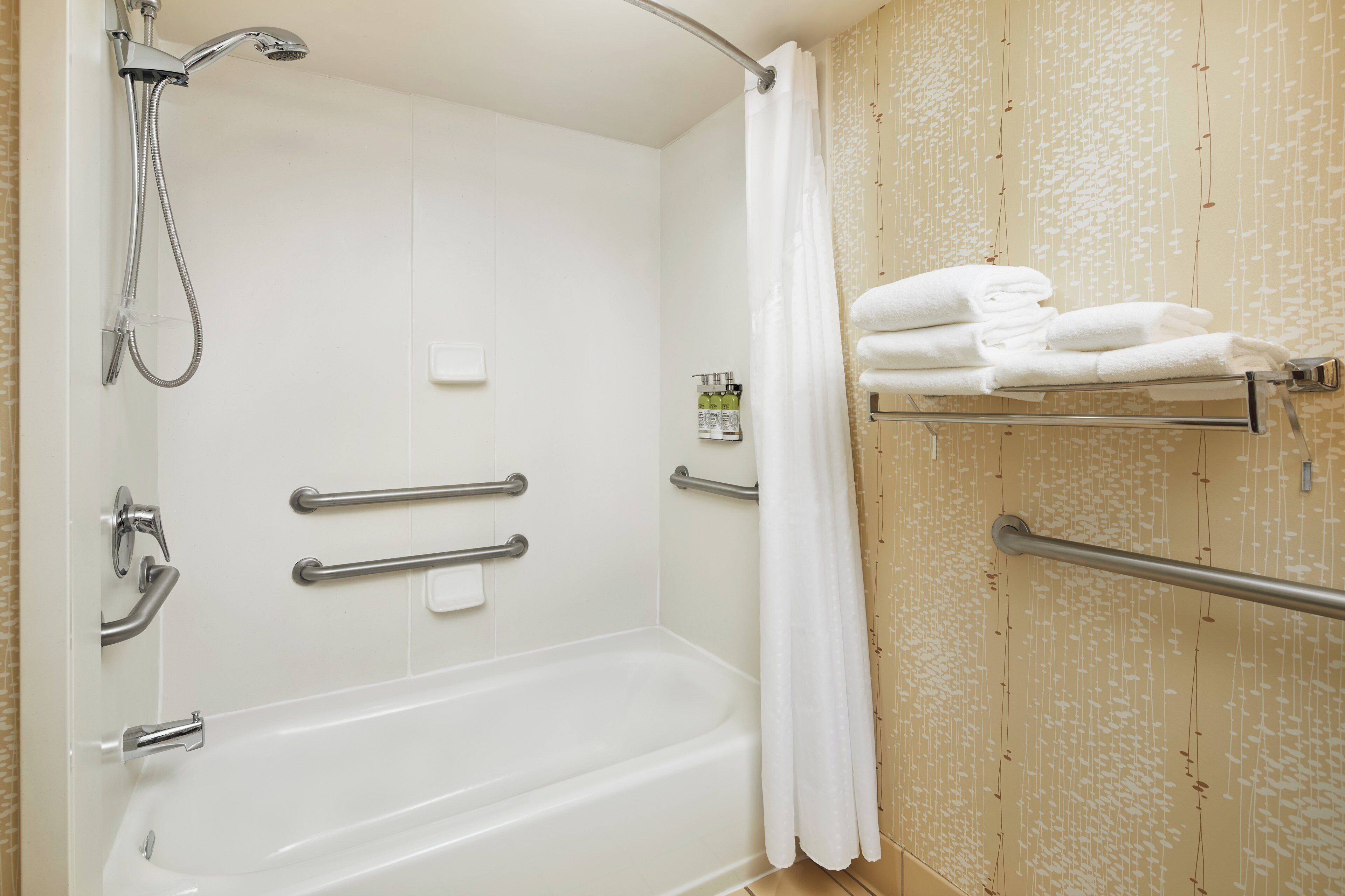 A bathroom with a bathtub, shower, handrails, and a towel rack.