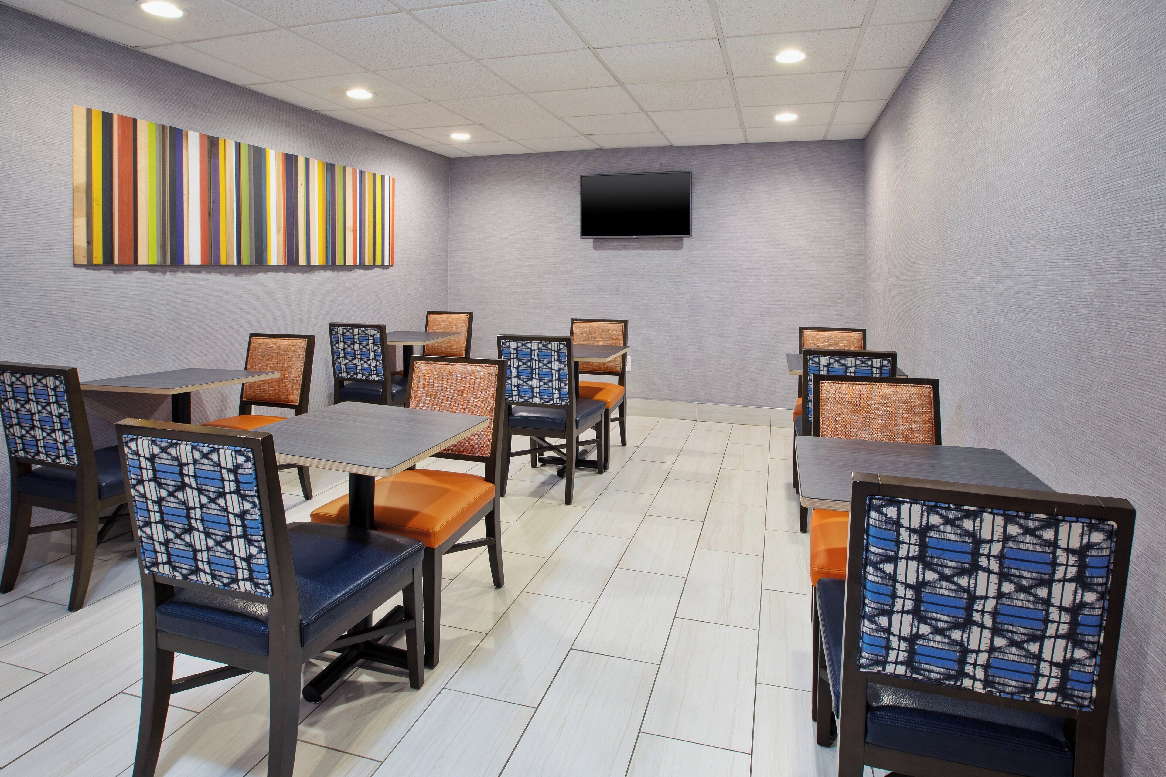 A conference room with tables and chairs, a flat-screen TV, and a colorful striped wall.