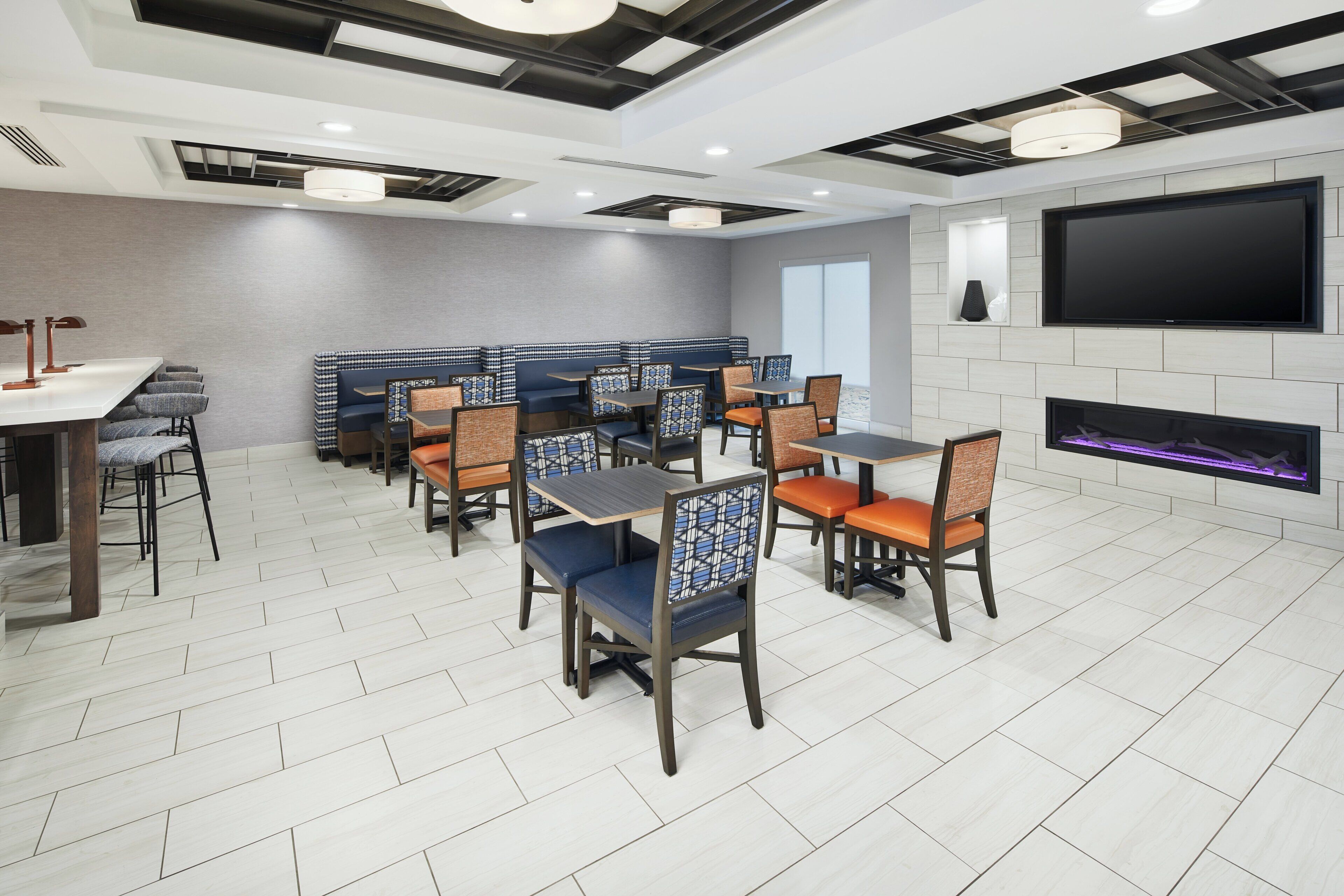 A modern dining area with multiple tables and chairs, a flat-screen TV, and a fireplace.