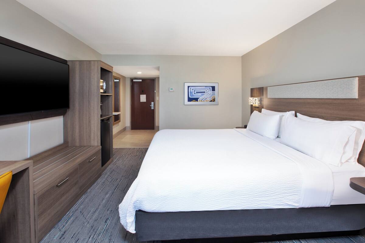 Une chambre d’hôtel dotée d’un grand lit, d’un téléviseur à écran plat, d’une armoire et d’une porte donnant sur un couloir.