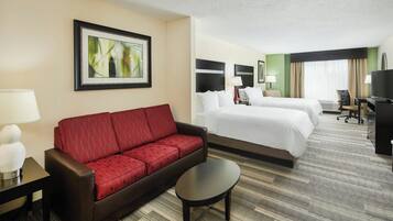 A hotel room with a red sofa, two beds, a desk, a TV, and a framed picture on the wall.