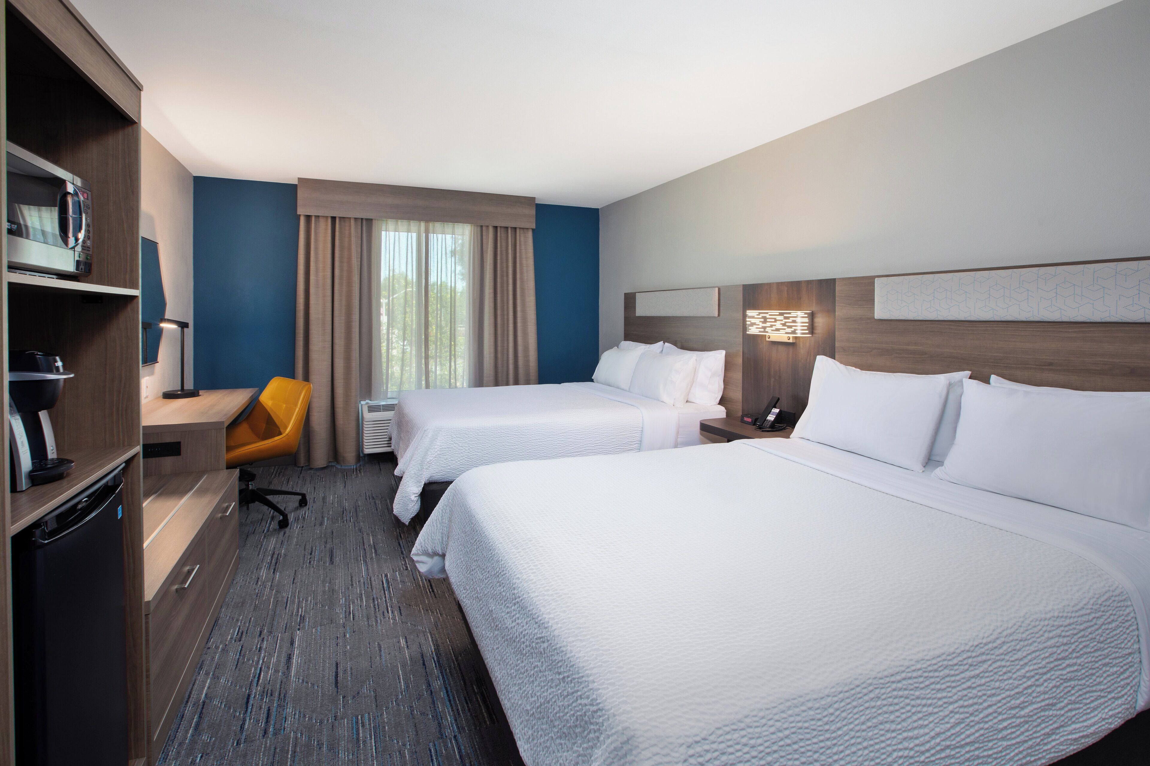 Una habitación de hotel con dos camas, un escritorio, una silla y un minibar.