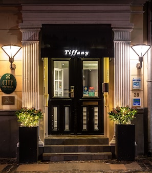 The exterior of a building with a black facade and the name 'Tiffany' above the entrance. There are two large potted plants at the entrance, and a sign indicating the building is part of the 'CITY HOTELS DENMARK' chain. - Hotel Tiffany (Copenhagen)