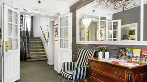 Um corredor com escada, cadeiras listradas, cômoda de madeira com livros e um espelho refletindo o ambiente.