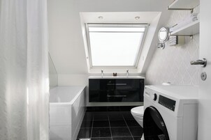 A compact bathroom with a skylight, a bathtub, a toilet, and a washing machine.