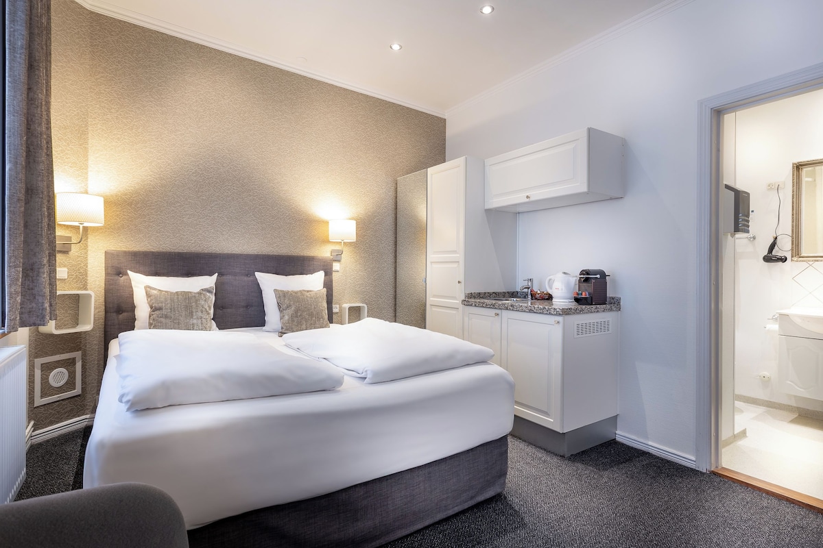 Una habitación de hotel con una cama grande, lámparas de noche, cafetera y armario.