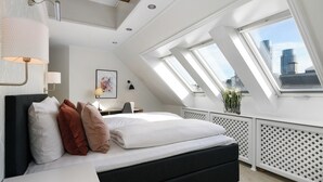 Quarto moderno com claraboia, cama, escrivaninha e vista para a cidade.