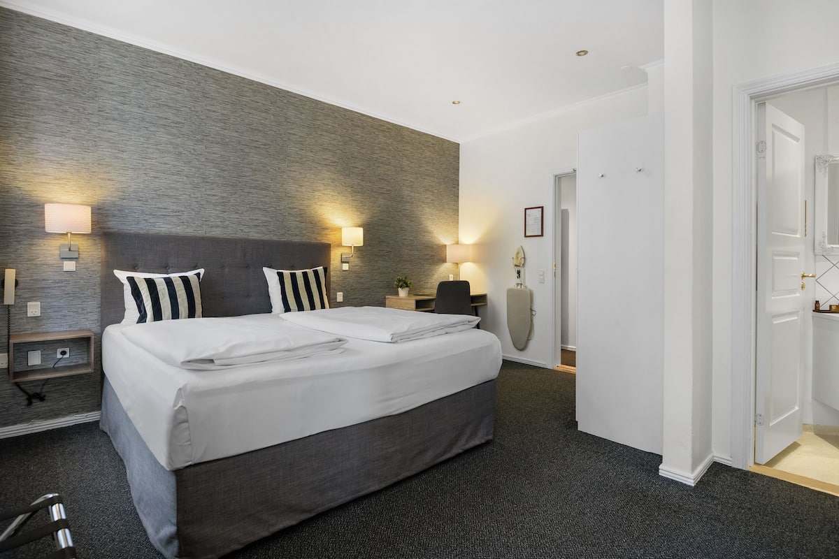 Una habitación de hotel con una cama grande, dos mesitas de noche, un escritorio y una silla.
