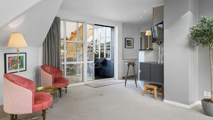 Uma sala de estar moderna com uma grande porta de vidro deslizante que dá para uma varanda, um banquinho de madeira e uma televisão sobre um suporte.