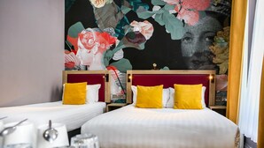 Habitación de hotel con dos camas, cada una con cabecero rojo y almohadas amarillas. En la pared detrás de las camas, hay una gran obra de arte floral.