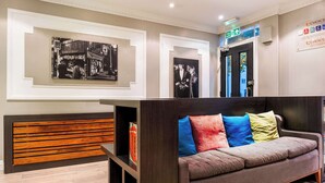 Un área de recepción moderna con un mostrador de madera, un sofá con cojines de colores y fotografías blanco y negro enmarcadas en las paredes.