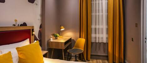 Habitación de hotel con cama, escritorio, silla, lámpara y ventana con cortinas.