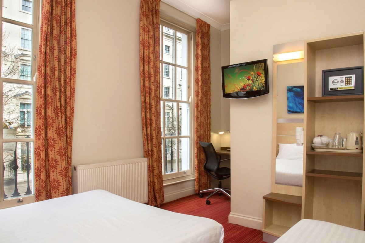 Habitación de hotel con dos camas, un escritorio, una silla, un televisor y un estante con artículos de aseo.