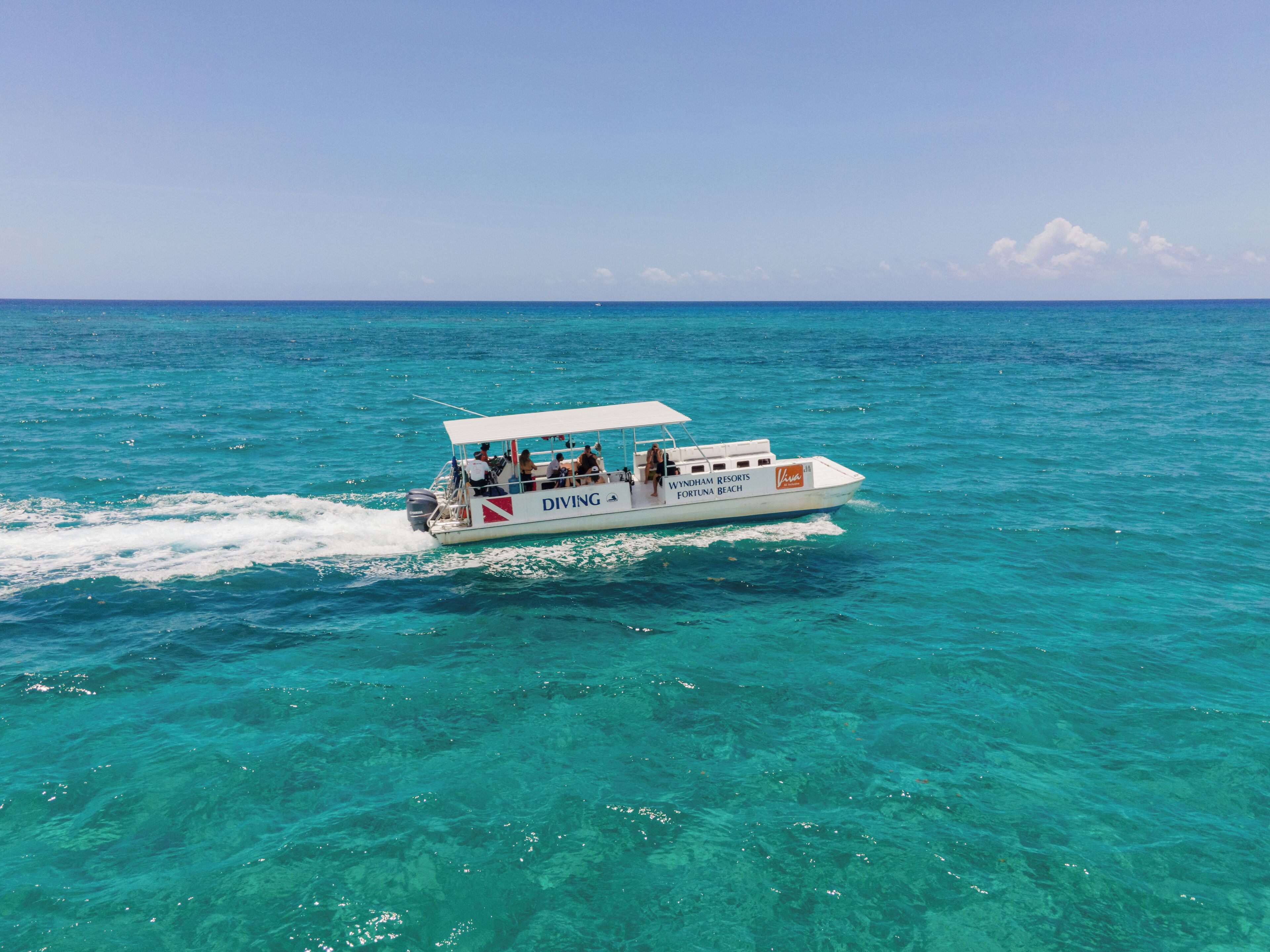 A boat with 'DIVING' and 'WYNDHAM RESORTS FORTUNA BEACH' written on it, moving through clear turquoise waters.