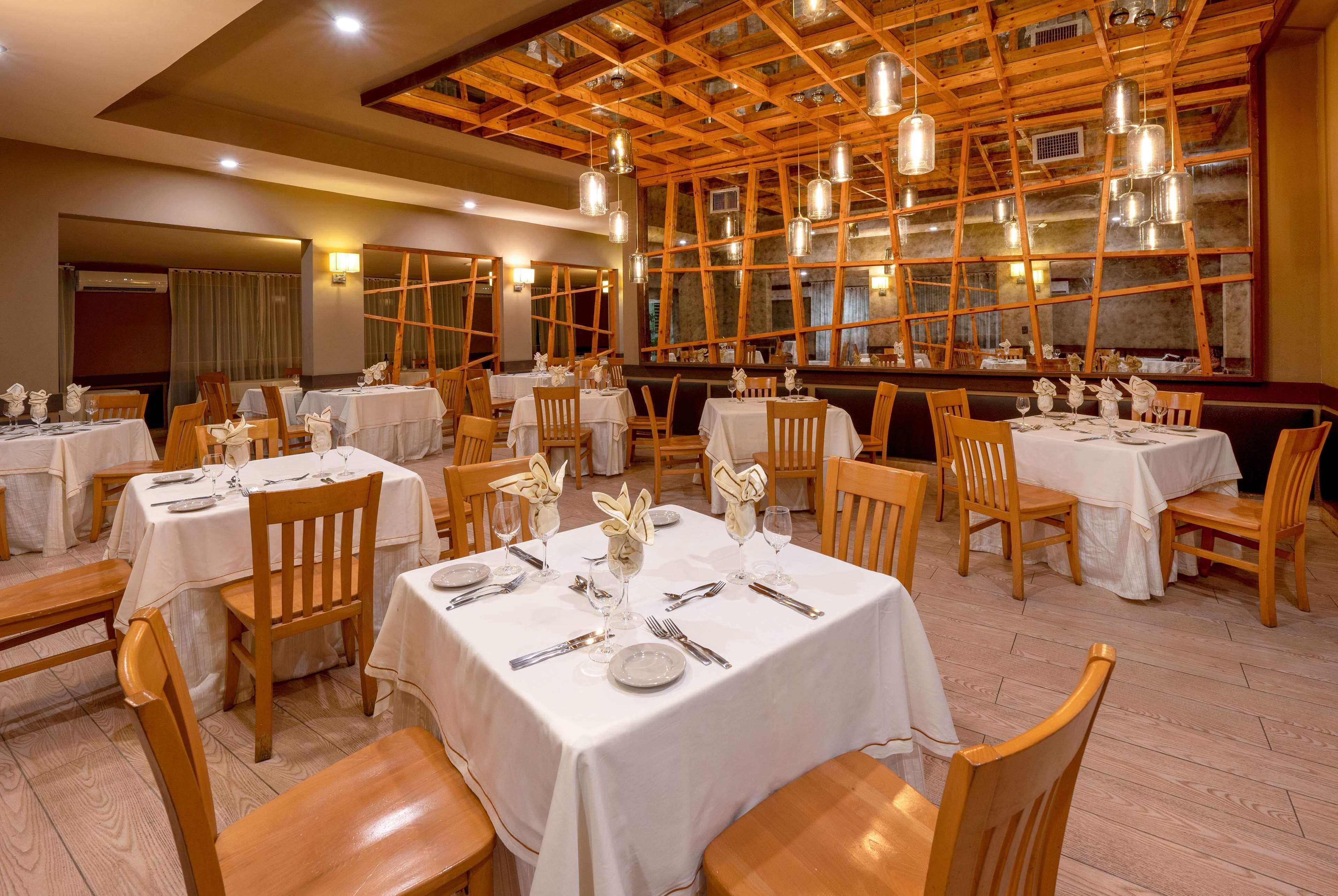 A restaurant with multiple tables set for dining, wooden chairs, and a rustic ceiling with exposed beams.
