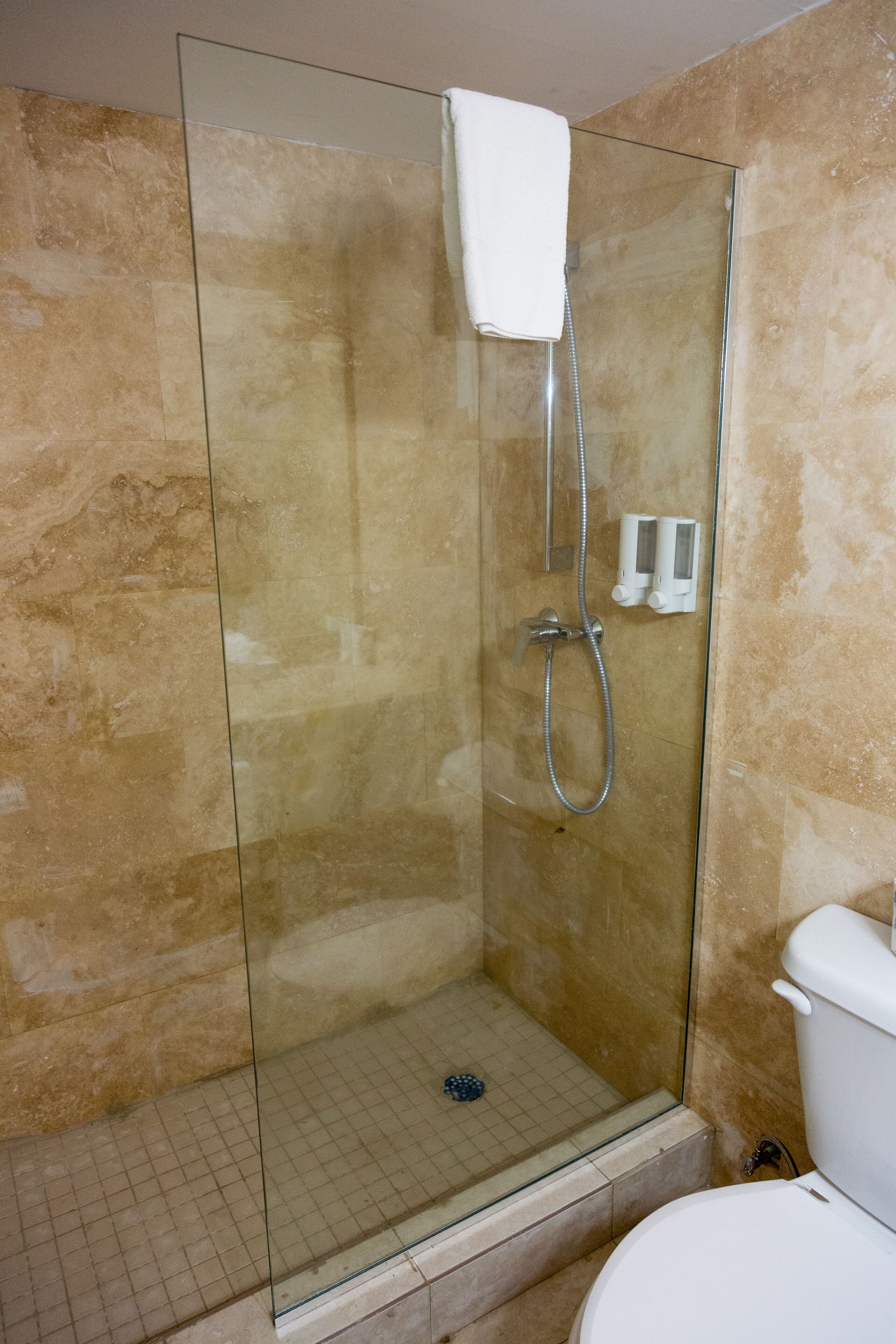 A glass-enclosed shower stall with a handheld showerhead and a white towel hanging on the wall.