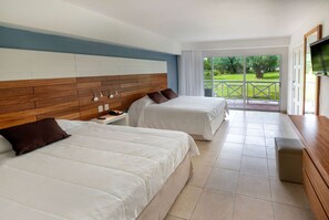 A hotel room with two beds, a wooden headboard, a TV, and a balcony with a view of greenery. - Viva Fortuna Beach by Wyndham, A Trademark Resort (Freeport)