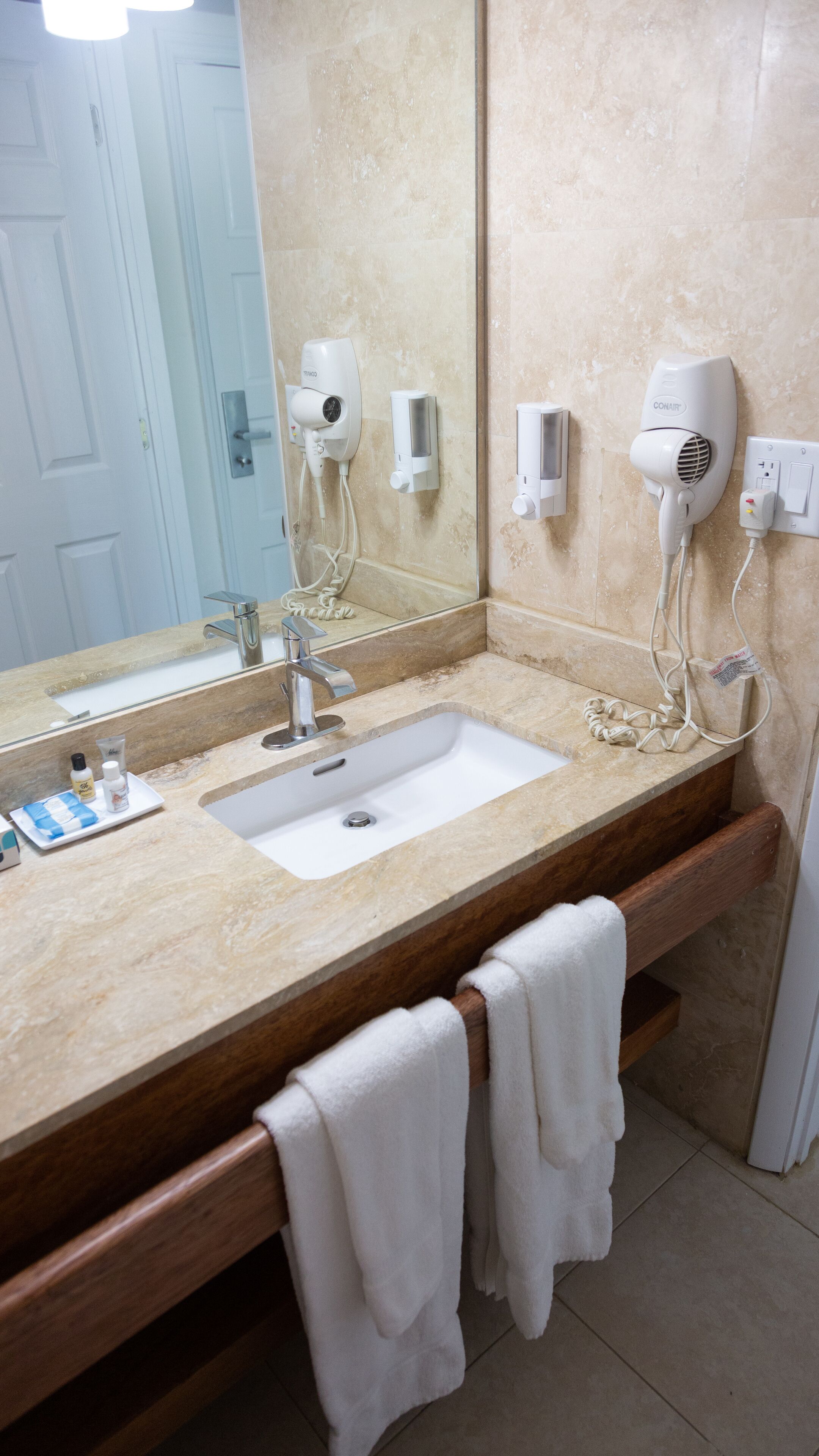 Une salle de bain équipée d’un lavabo, d’un miroir, d’un porte-serviettes et de sèche-cheveux.