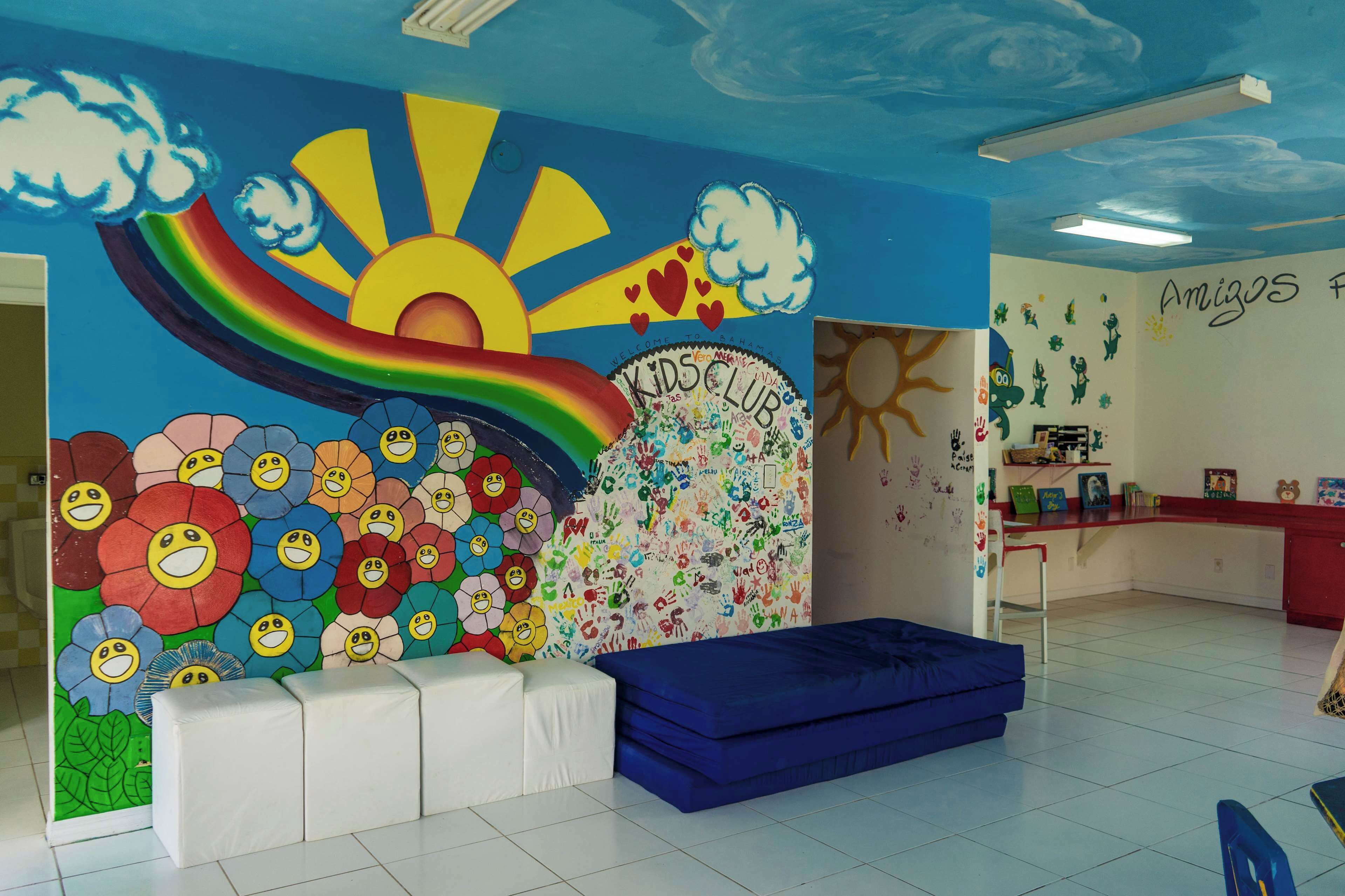 A children's play area with a colorful mural, a play mat, and a wall with children's artwork.