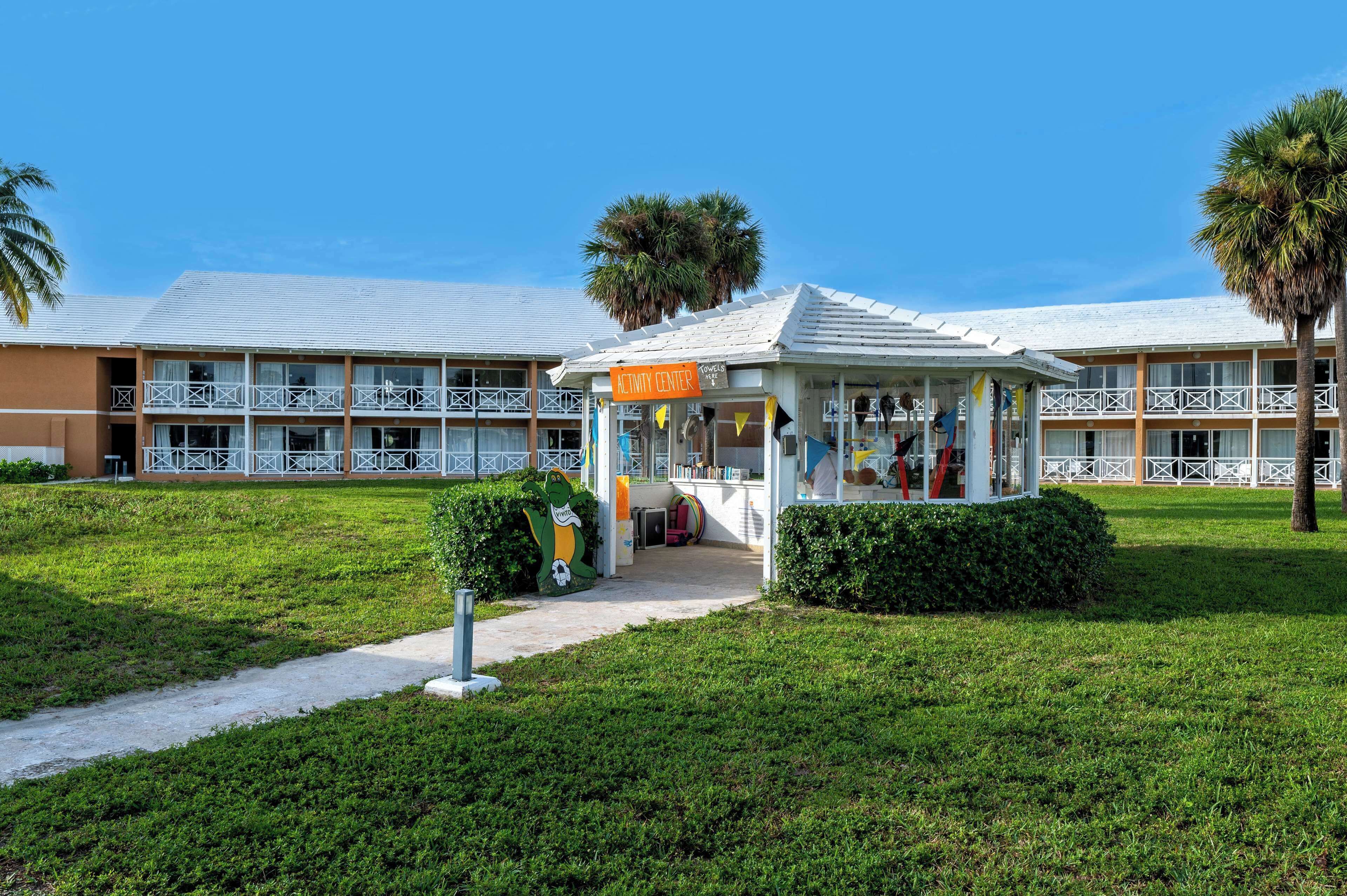 A hotel with a central activity center, multiple balconies, and a well-maintained lawn.