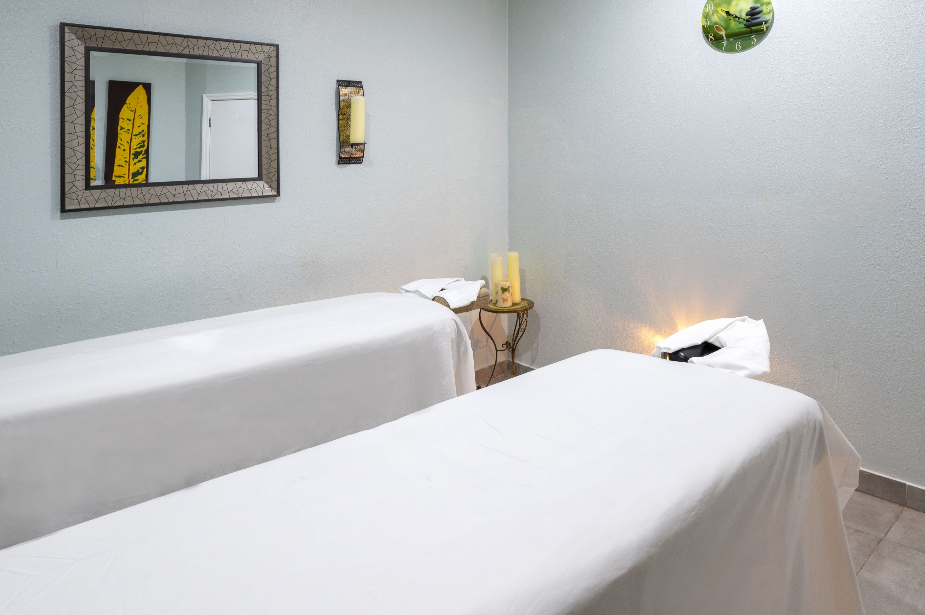 A room with two beds, a mirror, a small table with candles, and a wall clock.