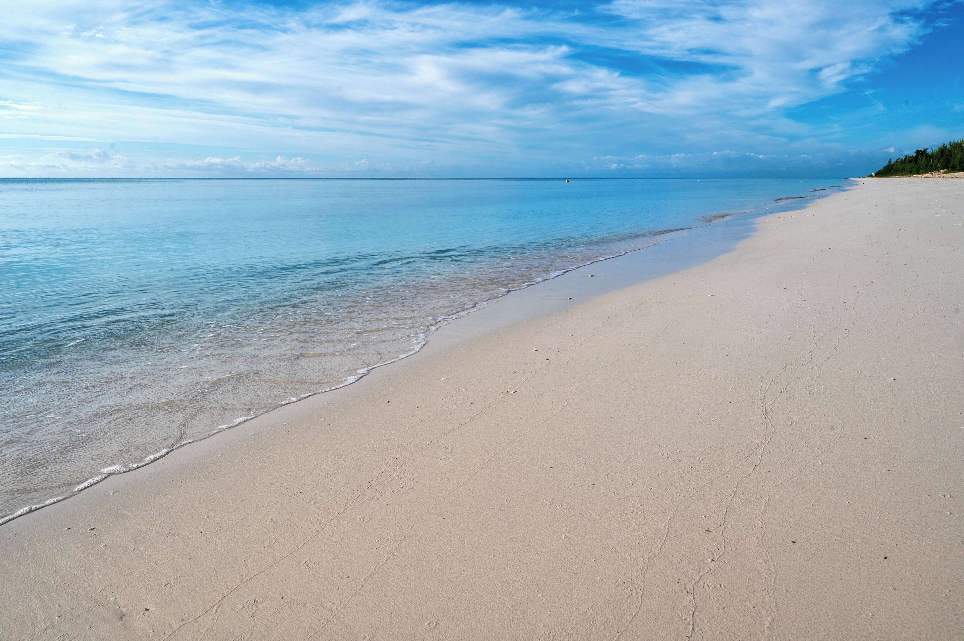 A wide sandy beach with gentle waves, a clear sky, and a distant horizon.