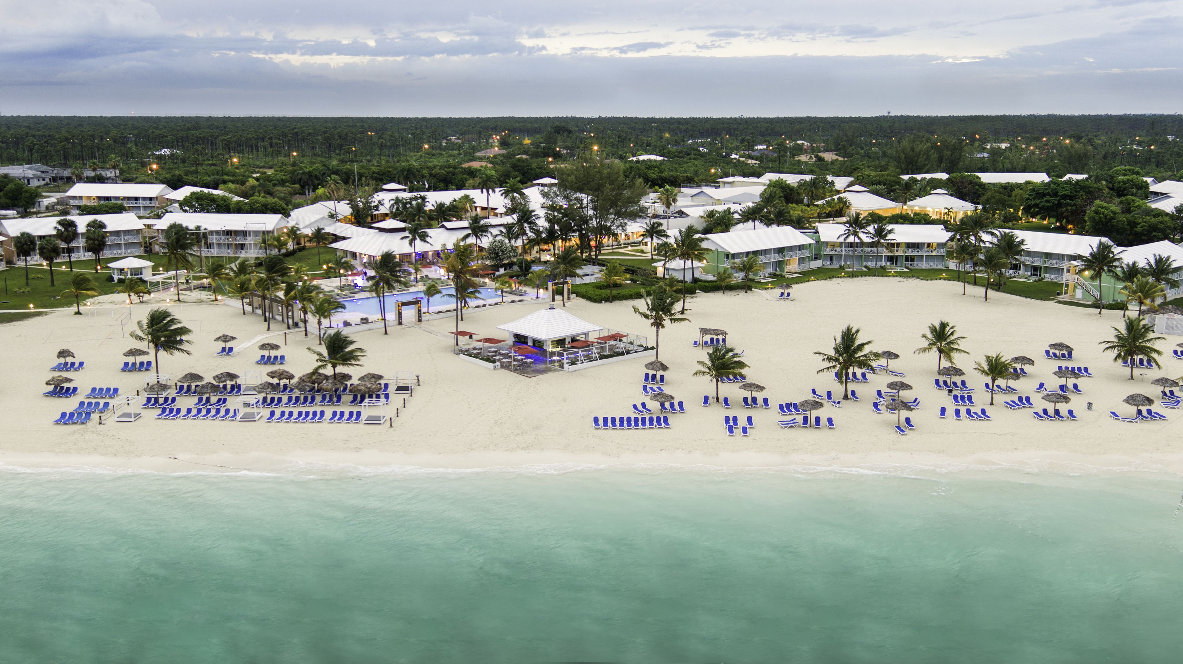 A resort with multiple buildings, a beach with sun loungers and umbrellas, and a pool area.