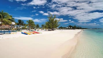 A beach with clear turquoise water, white sand, and palm trees.