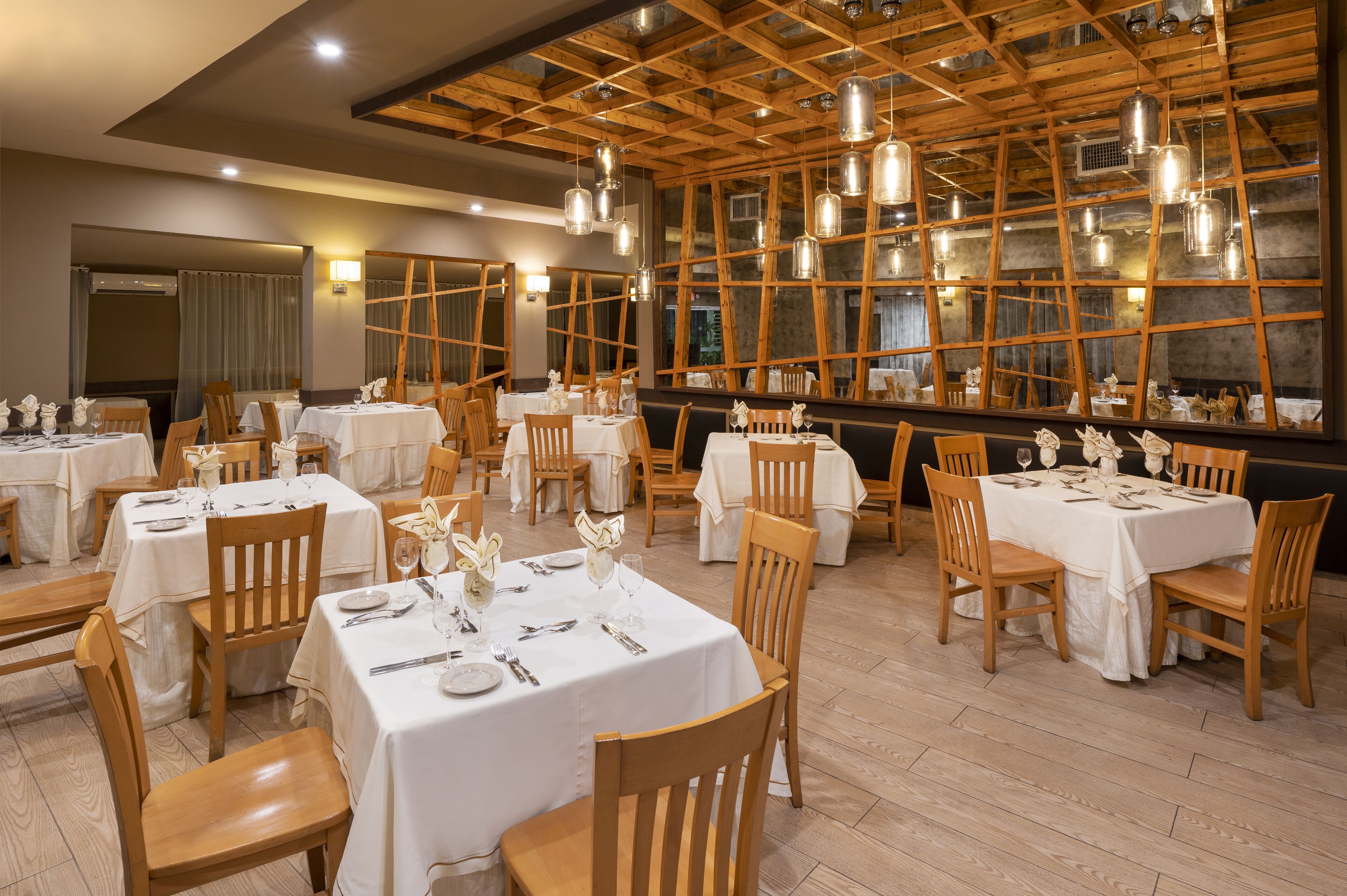 A restaurant with wooden beams and hanging light fixtures, tables set with white tablecloths and chairs.