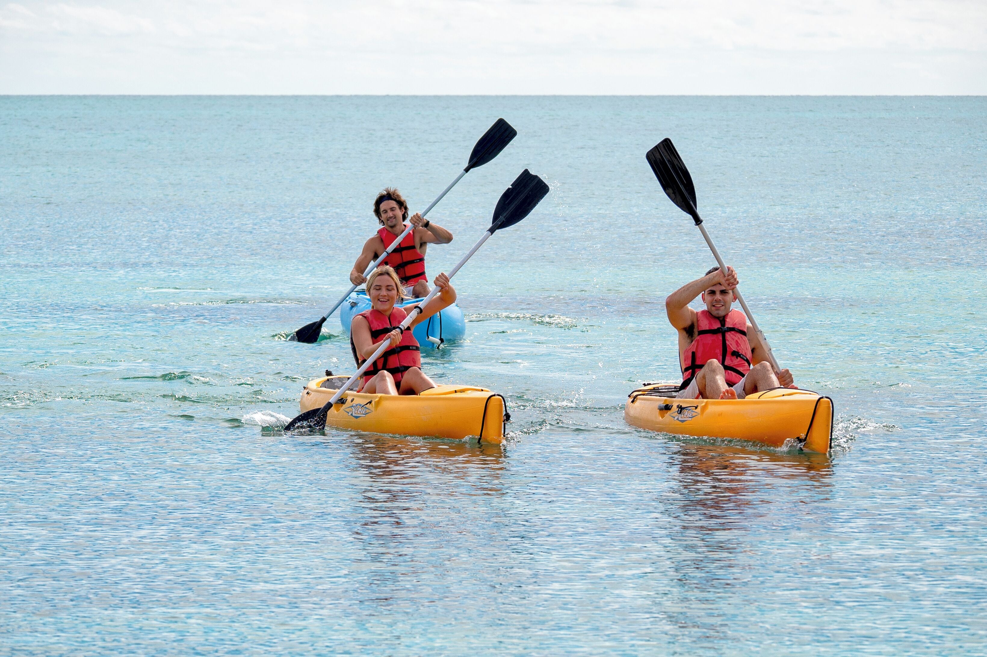 Three people in yellow inflatable kayaks on calm water.