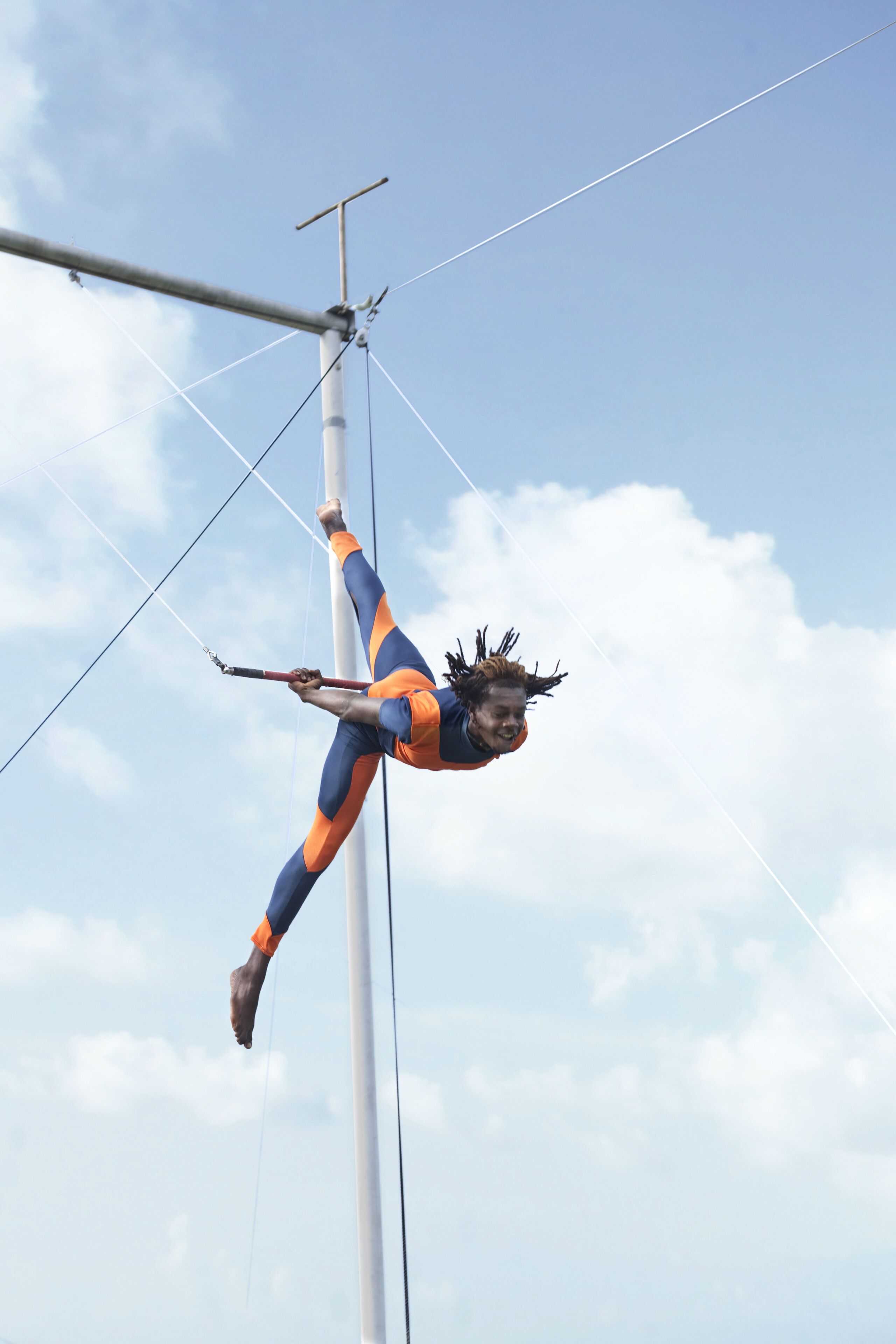 A trapeze artist performing on a high bar against a clear sky.