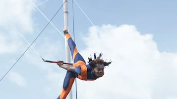 A trapeze artist performing on a high bar against a clear sky.