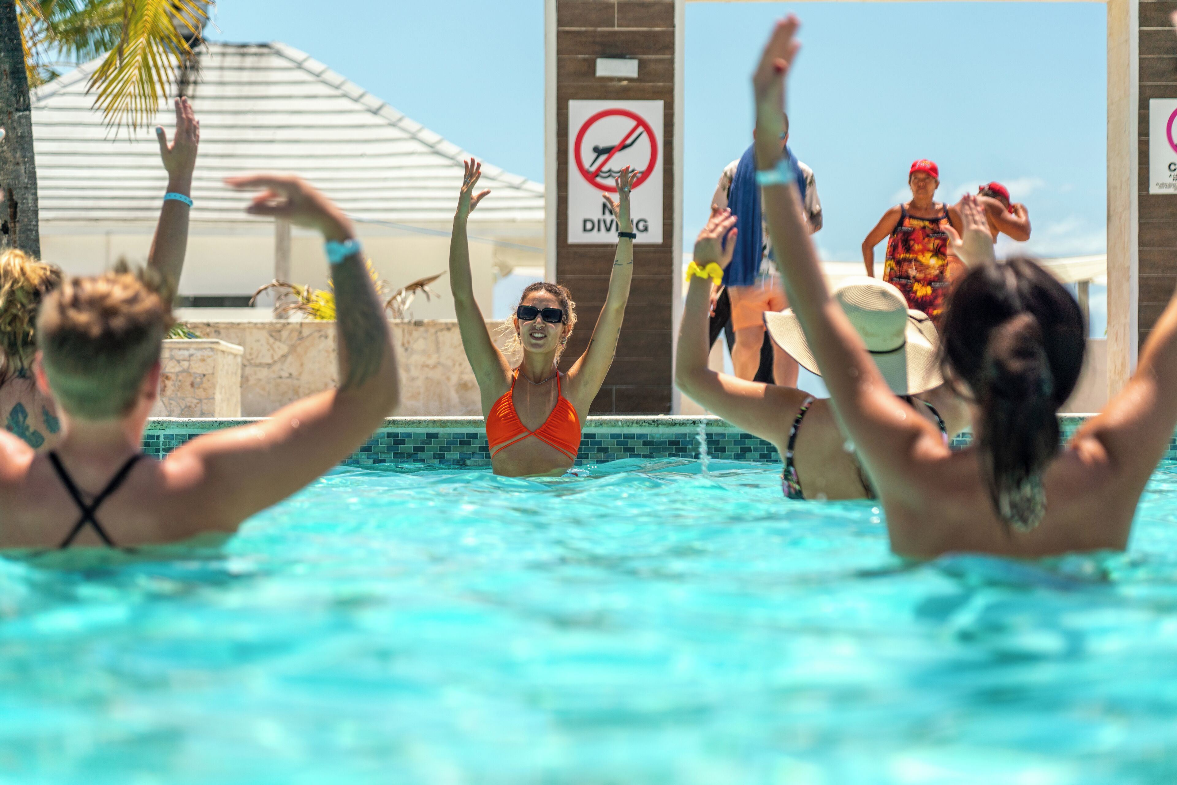 Ein Poolbereich mit einem 'No Diving'-Schild, blauem Himmel und Personen im Wasser.