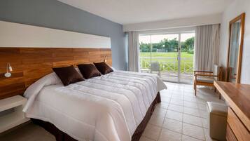 A hotel room with a large bed, wooden headboard, and a view of a grassy area through a sliding glass door.