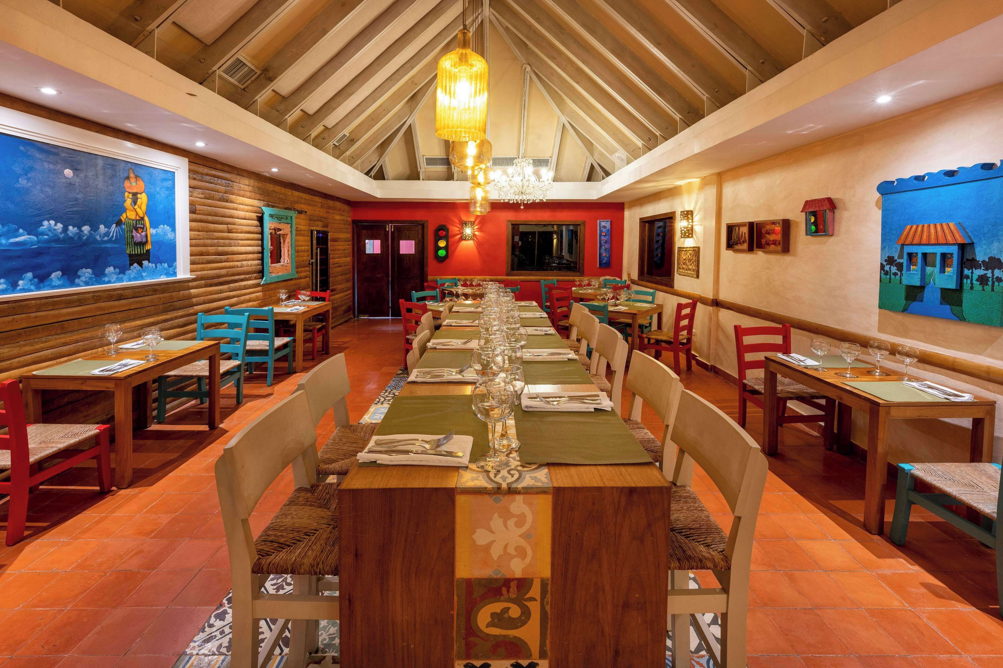 Ein Restaurant mit einem langen Holztisch, gedeckten Plätzen, Holzwänden und einer hohen Decke mit freiliegenden Balken.