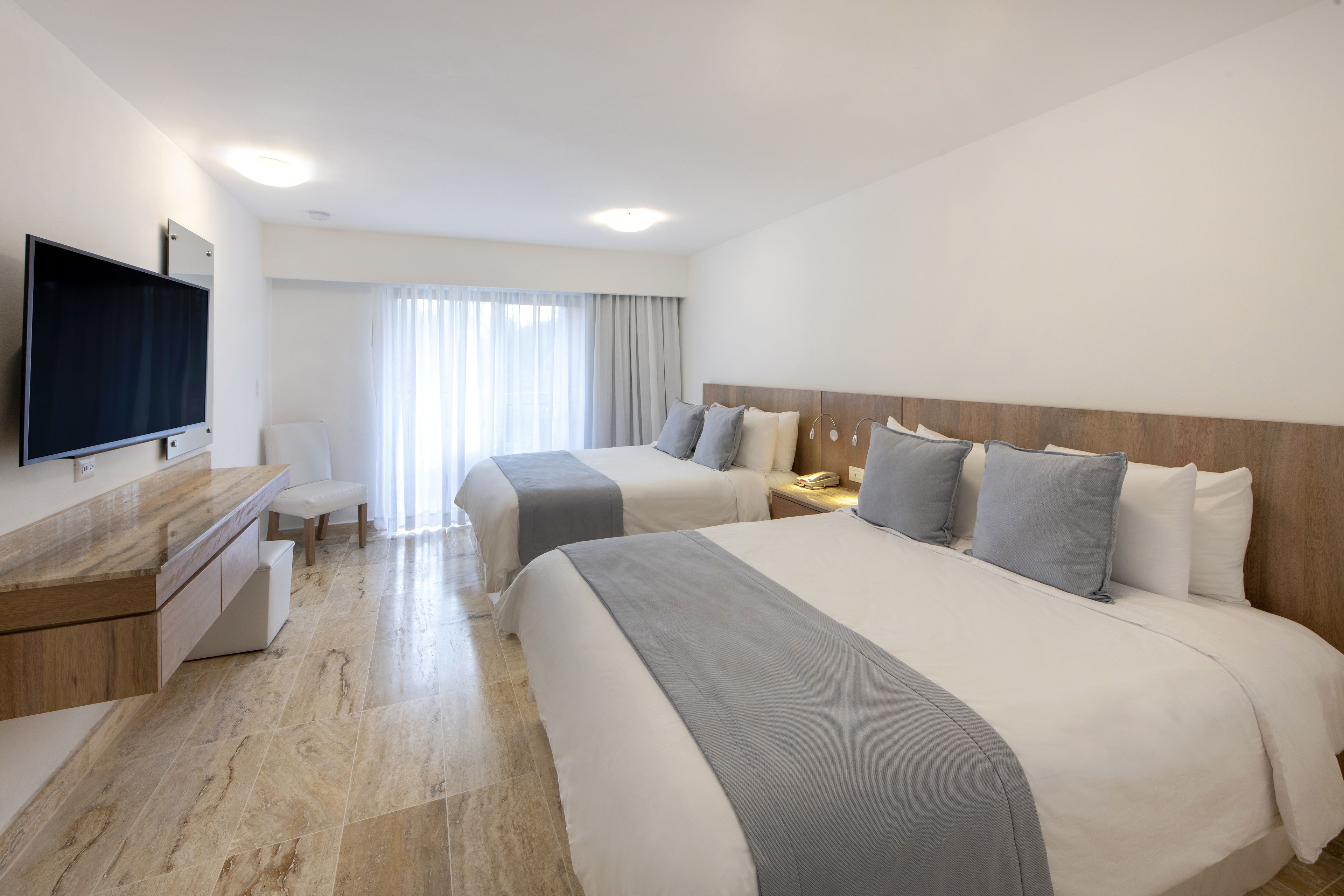 A hotel room with two beds, a TV, a desk, and a chair.