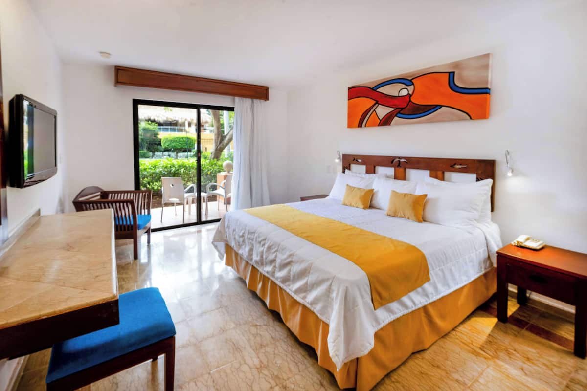 A hotel room with a bed, a desk, a chair, a TV, and a painting on the wall.