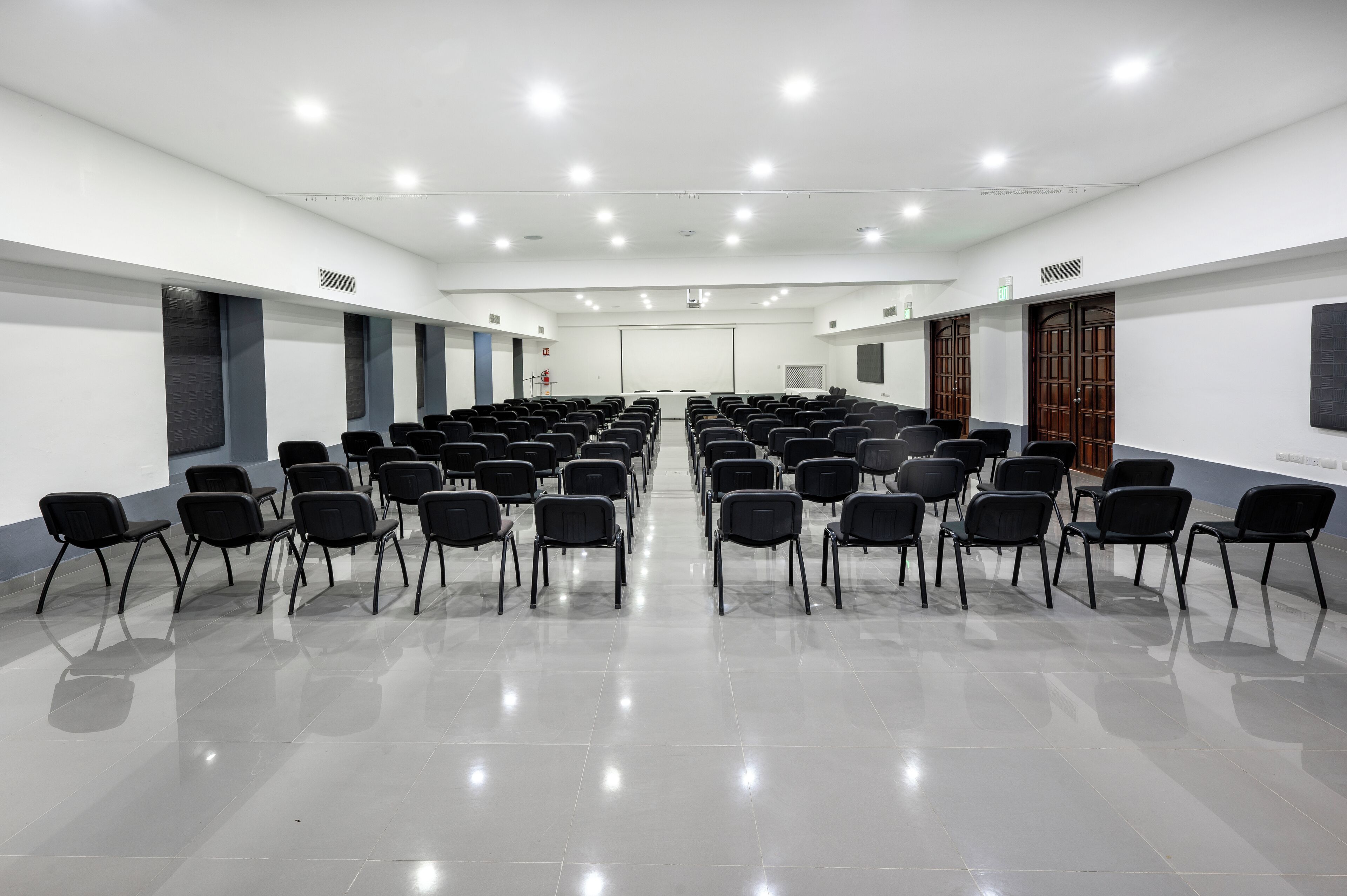 Une salle de conférence avec des rangées de chaises, un écran de projection et un tableau blanc.