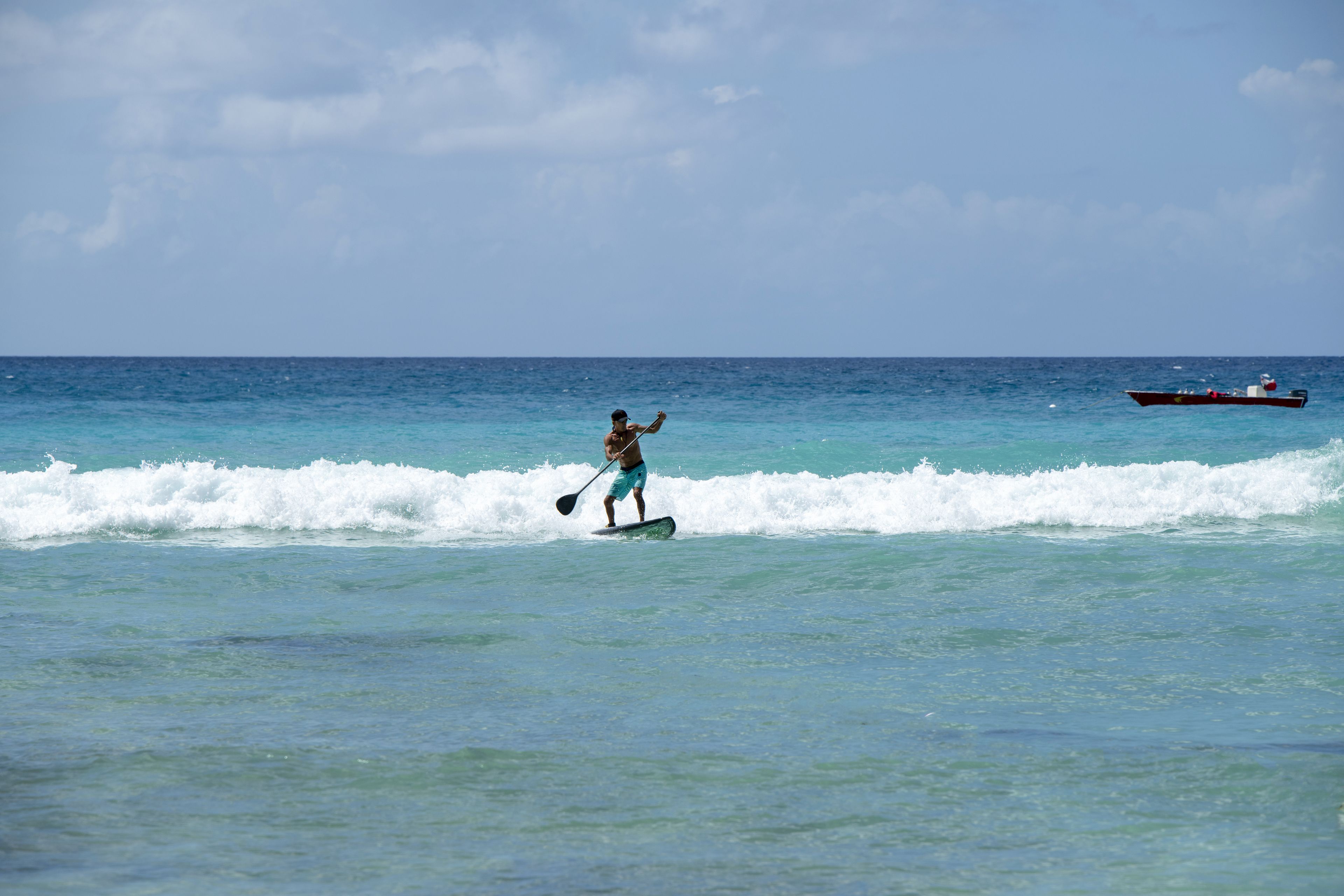 A person paddleboarding on the ocean with a boat in the background.