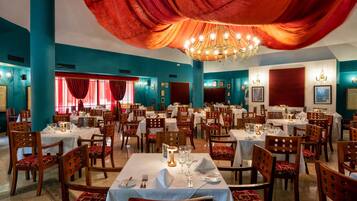 A restaurant with multiple tables and chairs, red curtains, and a chandelier.