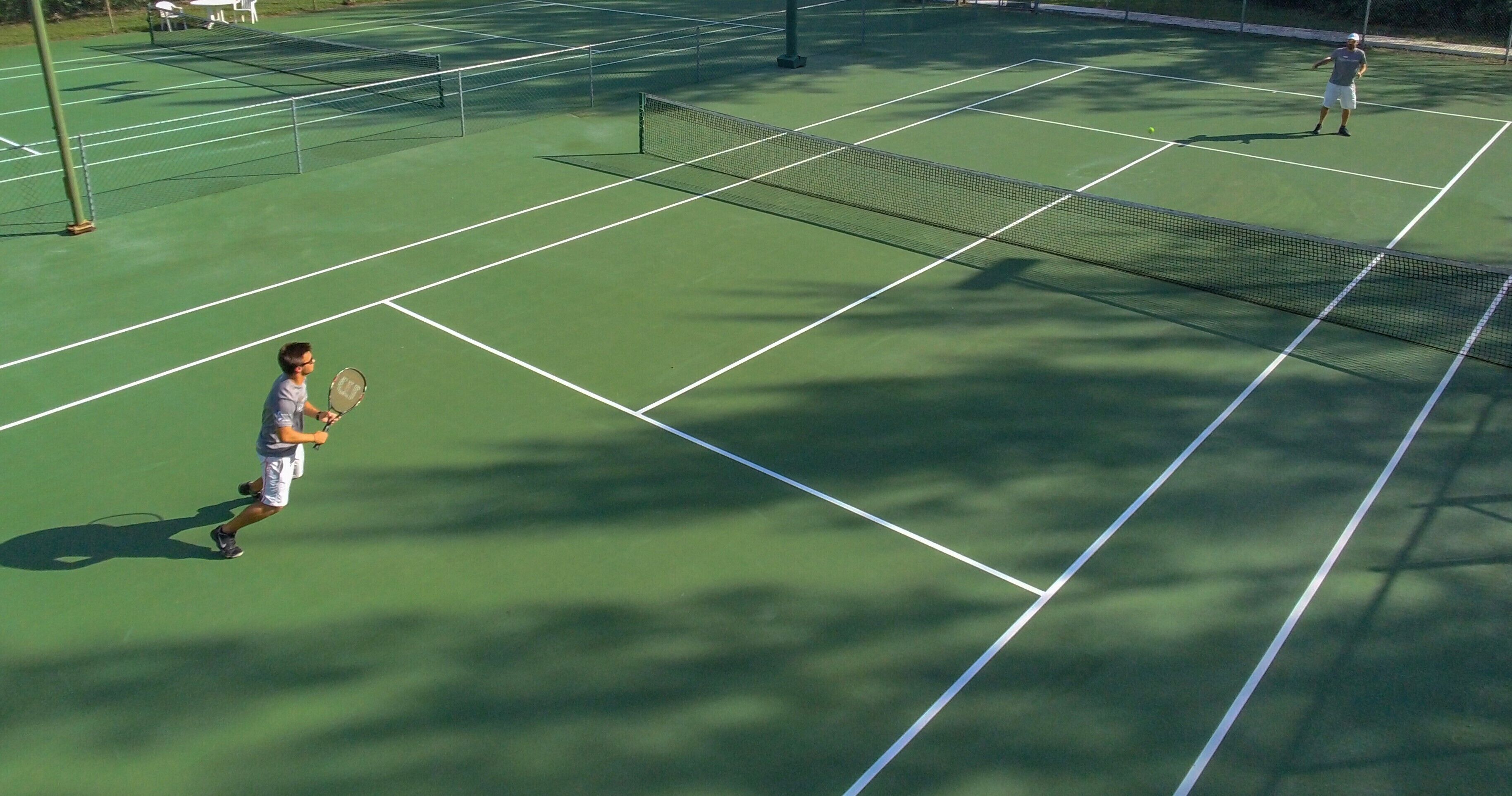 Een tennisbaan met net, lijnen en een bewegende speler.