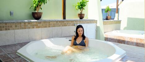 A woman in a hot tub with tiled flooring and potted plants.