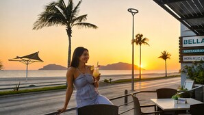 A woman at a seaside restaurant with a view of the sunset and palm trees.