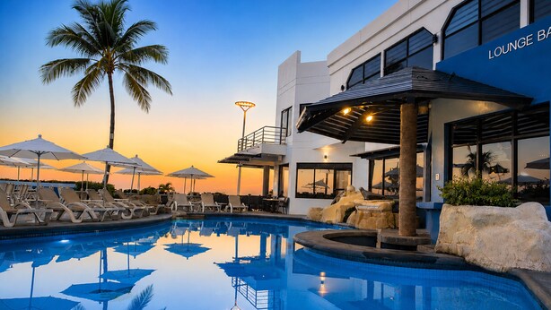 A pool area with lounge chairs and umbrellas, a palm tree, and a building labeled 'LOUNGE BAR'.