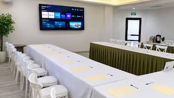 A conference room with a long table, chairs, a projector screen displaying a smart TV interface, and an exit sign on the wall.