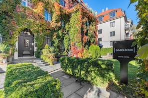 A hotel entrance with a black door, a sign reading "GABELSHUS HOME HOTEL," and a garden with neatly trimmed bushes. - Home Hotel Gabelshus (Oslo)