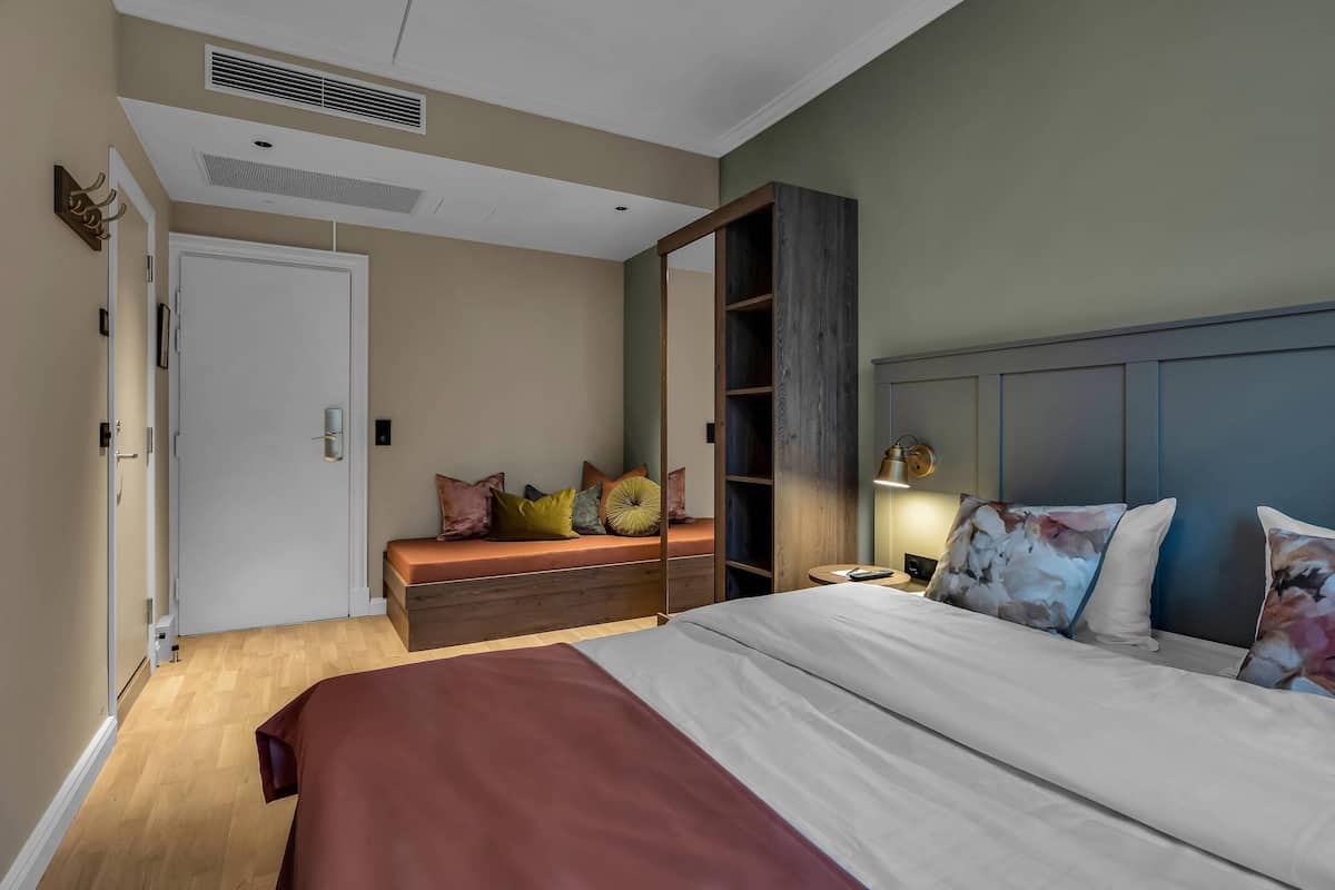 A bedroom with a large bed, a bench with cushions, a wardrobe, and a door.